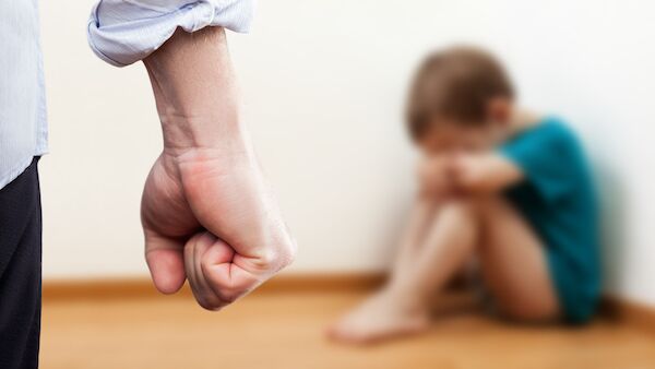 Adult clenching fist with young child in the background as an example of a violation of Colorado child abuse laws per CRS 18-6-401