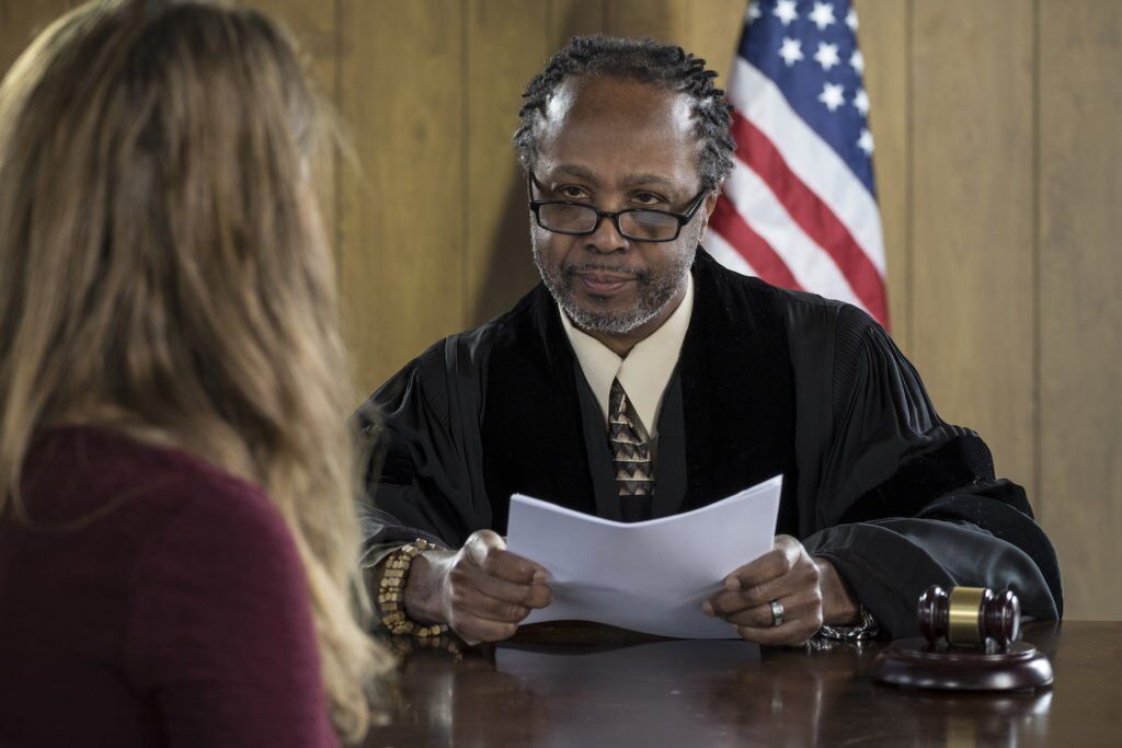 Judge at parole violation hearing speaking to defendant with a flag in the background