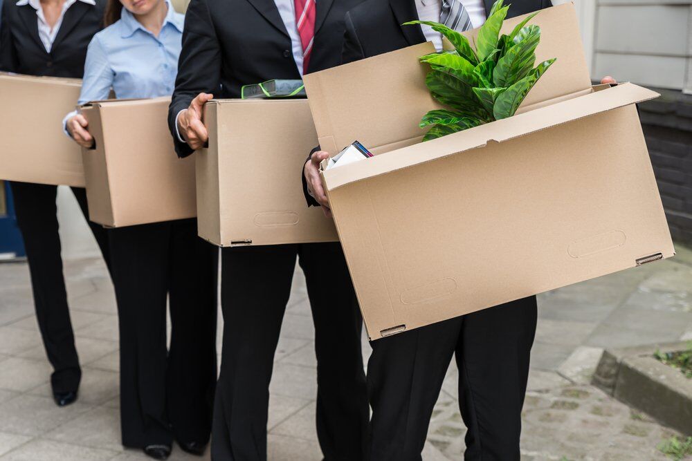 A large group of employees leaving an office building with their belongings.